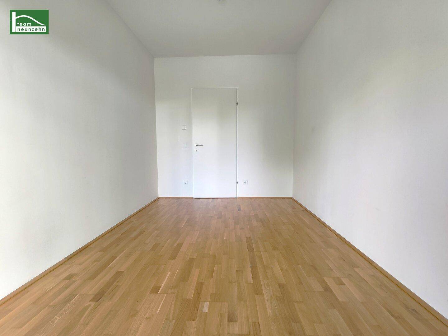 Geräumiges, leeres Schlafzimmer mit Holzboden und weißen Wänden.