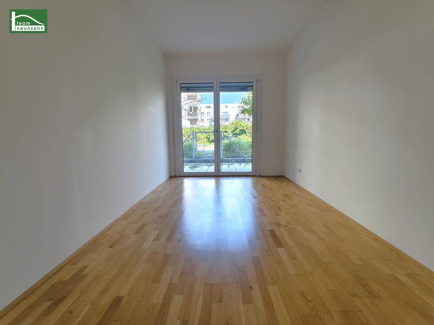 Geräumiges, helles Wohnzimmer mit Holzboden und großem Fenster zum Außenbereich.