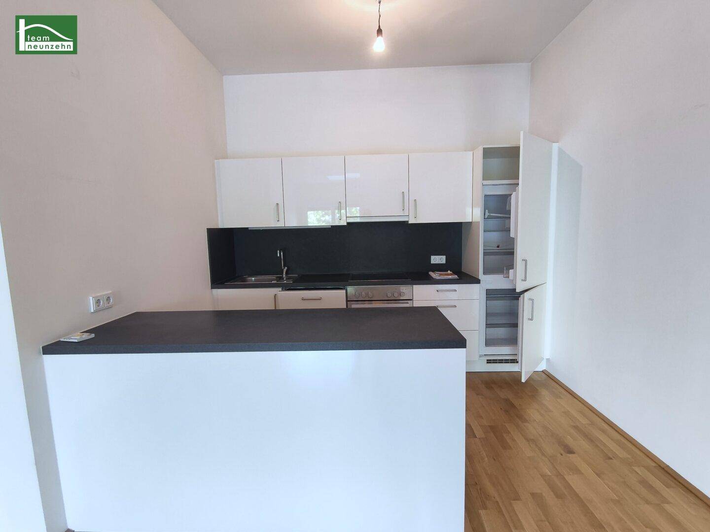 Moderne Küchenzeile mit weißen Hochglanzschränken, dunkler Arbeitsplatte und integriertem Kühlschrank.