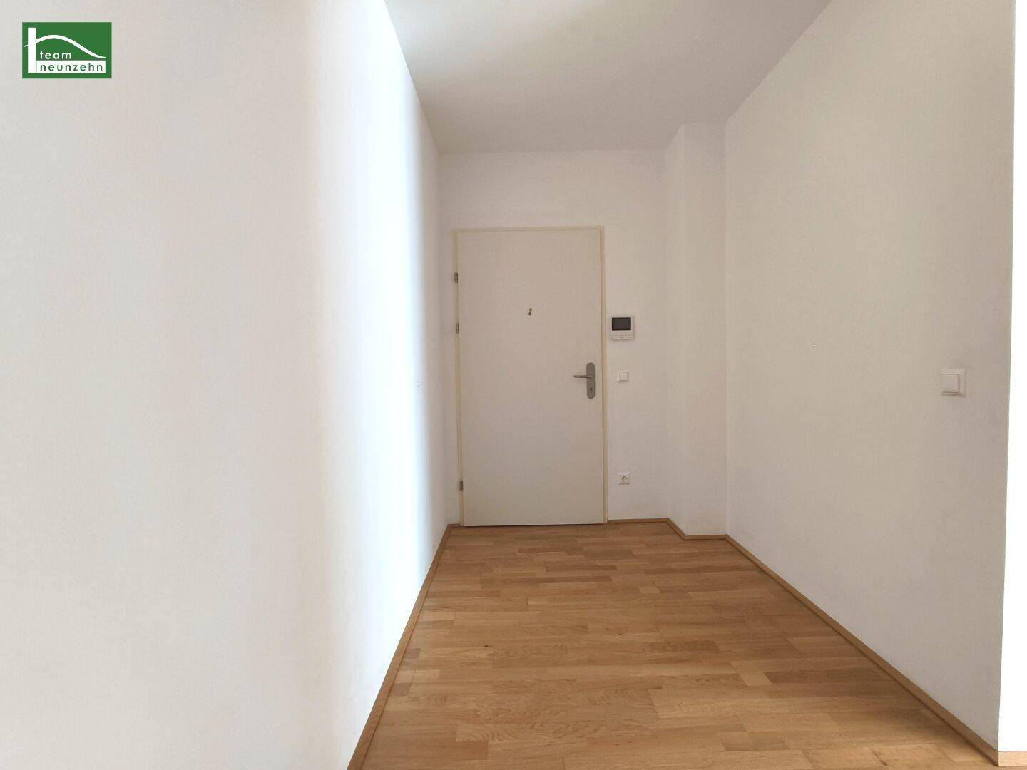 Heller Eingangsbereich mit Parkettboden und weißer Eingangstür.