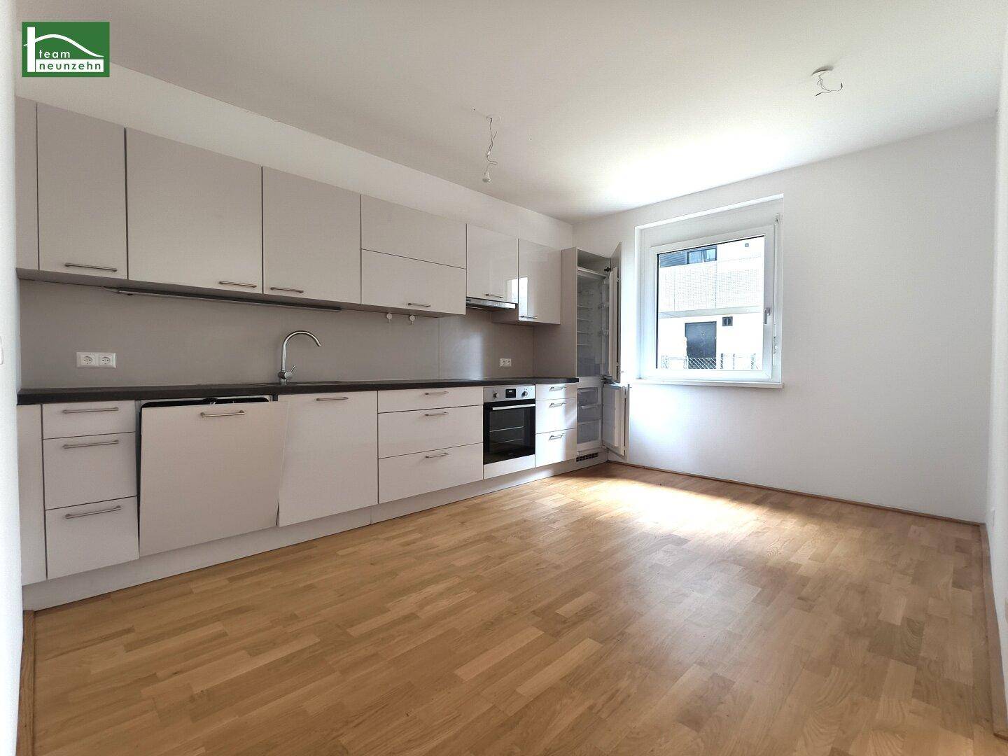 Moderne Einbauküche mit hellen Schränken, integrierten Geräten und Fenster.