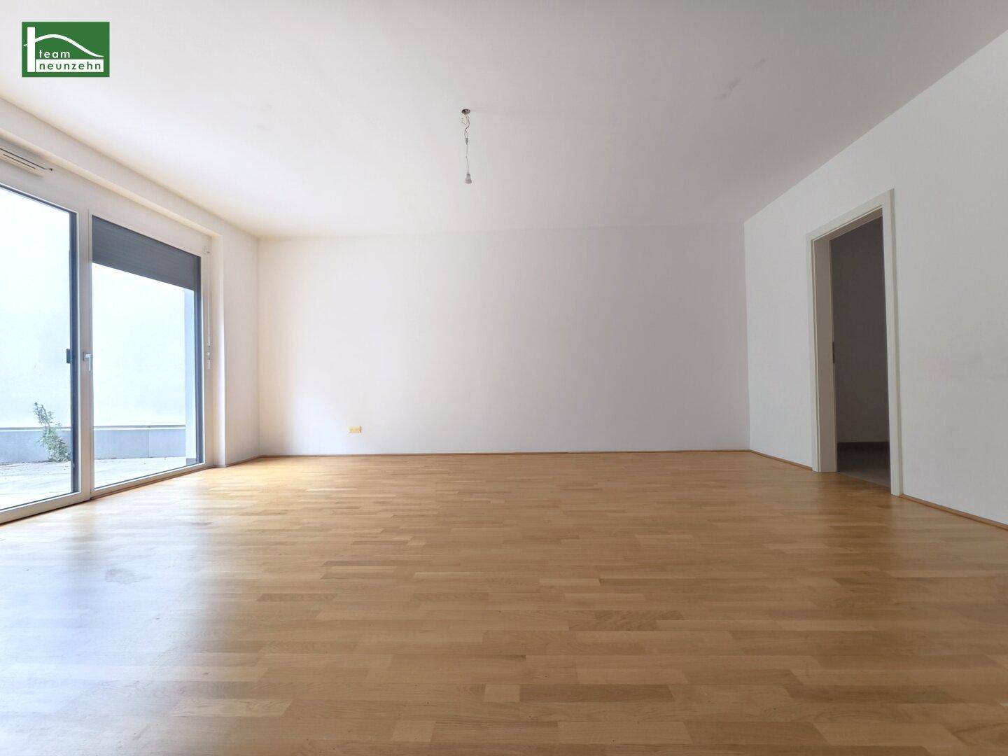 Leeres Wohnzimmer mit Parkettboden und Schiebetür zu einem Außenbereich.