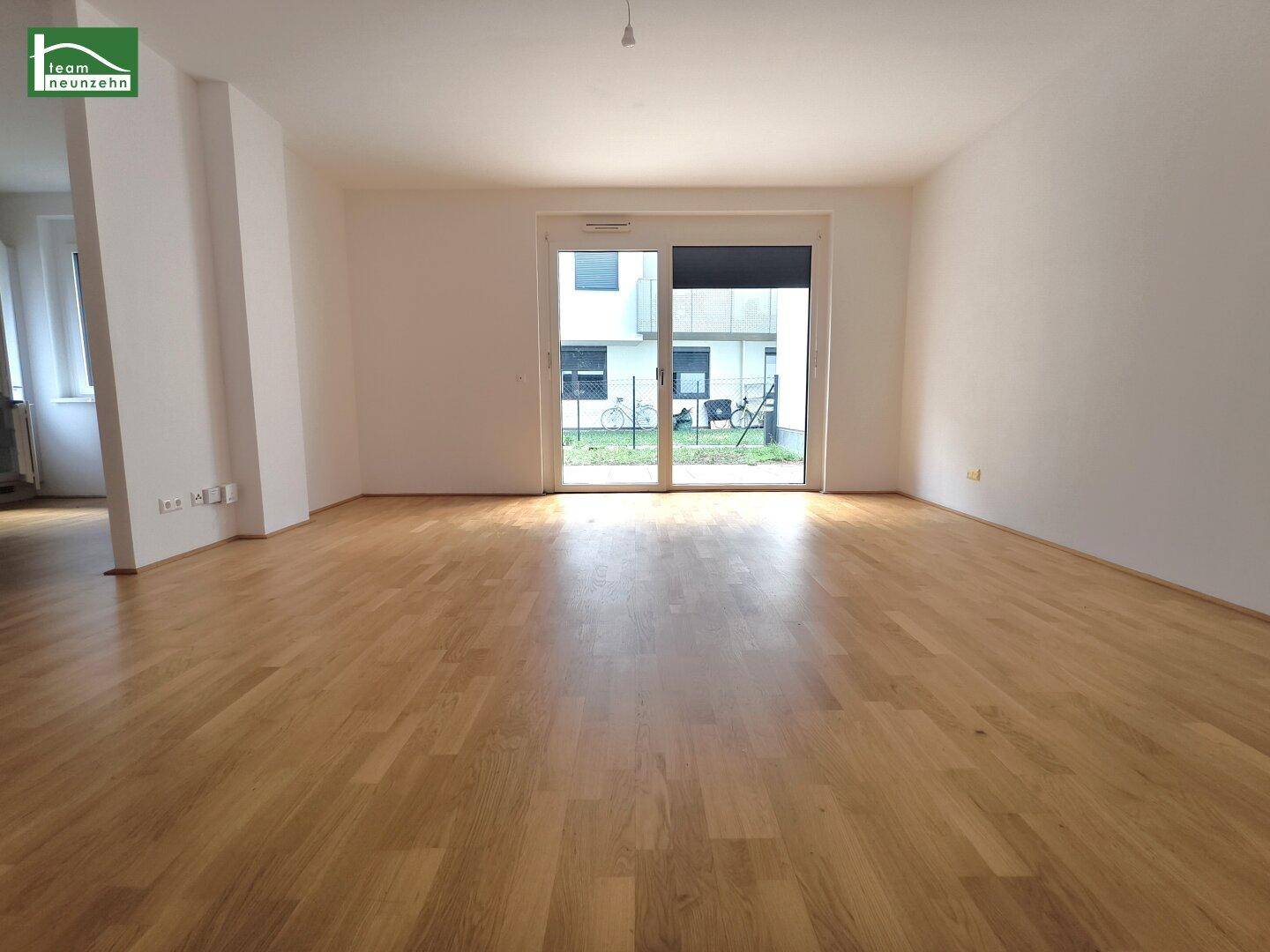 Geräumiges Wohnzimmer mit hellem Parkettboden und großen Fenstern zum Außenbereich.