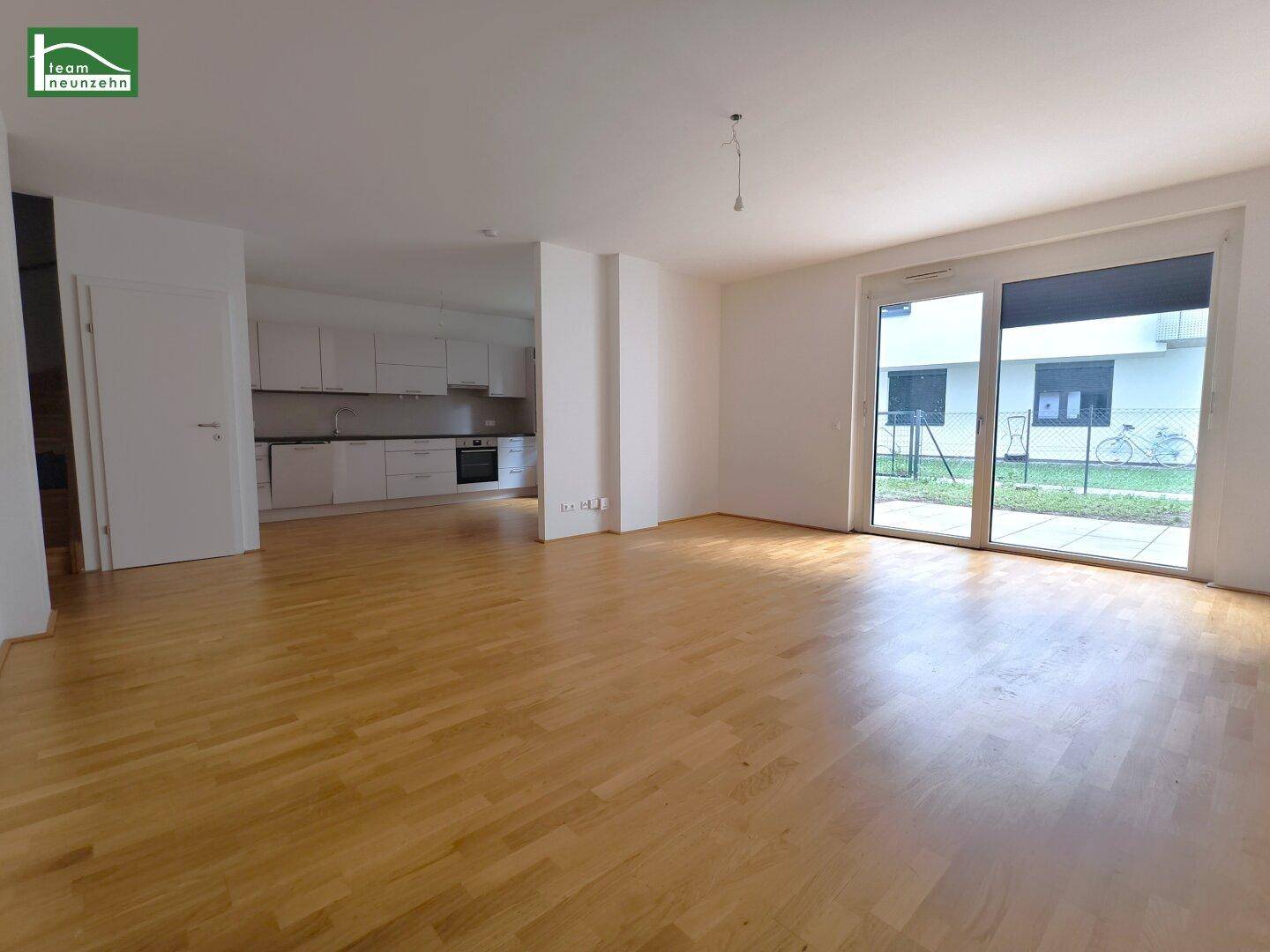 Heller offener Wohnbereich mit Parkettboden und Zugang zu einer kleinen Terrasse.