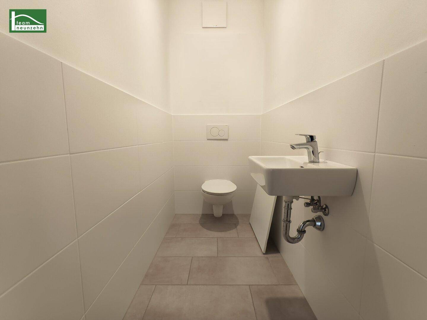 Modernes Gäste-WC mit Wand-WC, kleinem Waschbecken und Fliesenboden.