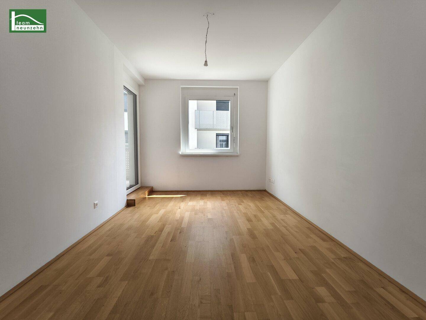 Helles Schlafzimmer mit Parkettboden und einem Fenster mit Blick nach draußen.