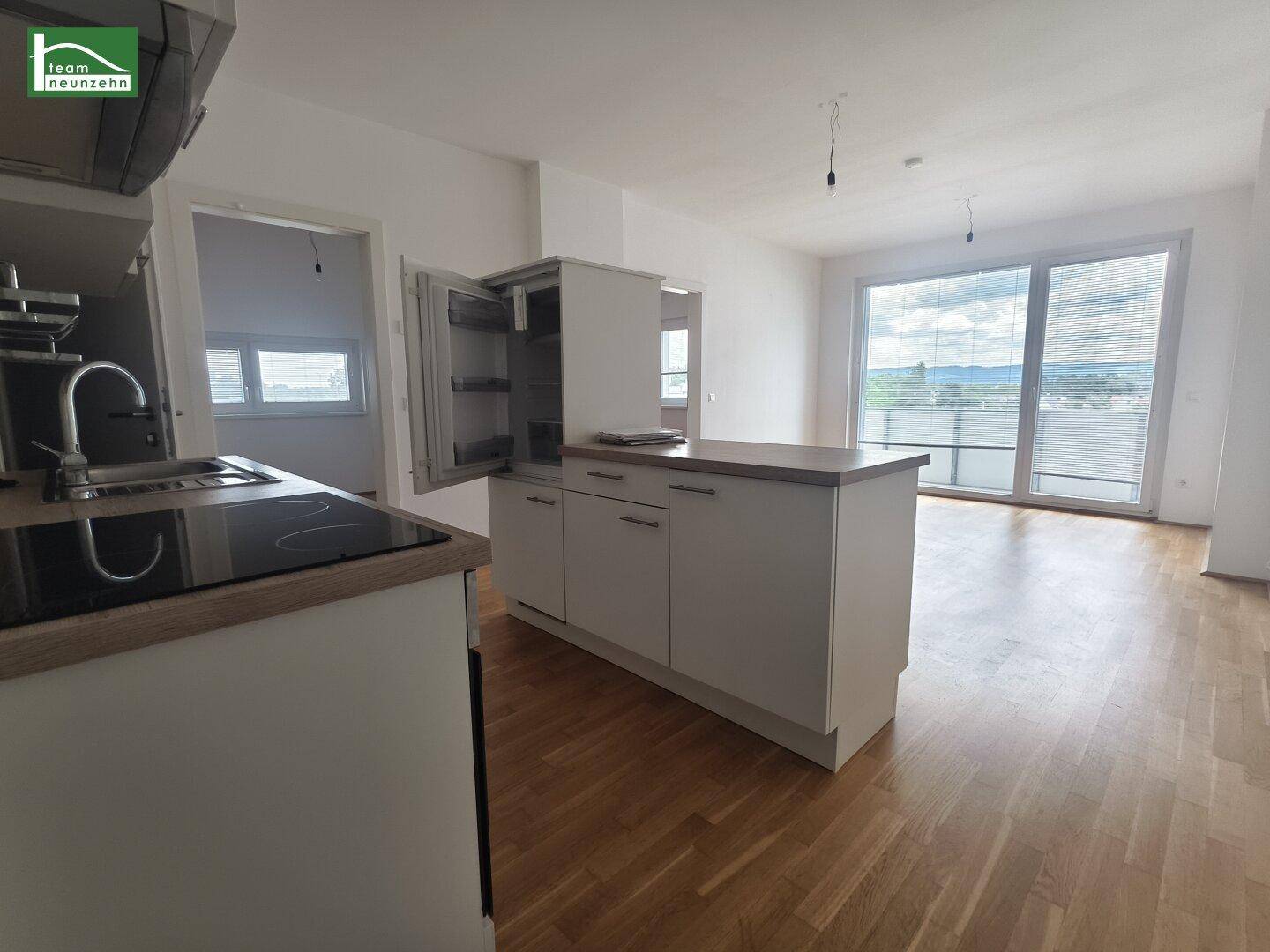 Moderne offene Küche mit Holzarbeitsplatte, integriertem Kühlschrank und Blick ins Wohnzimmer.