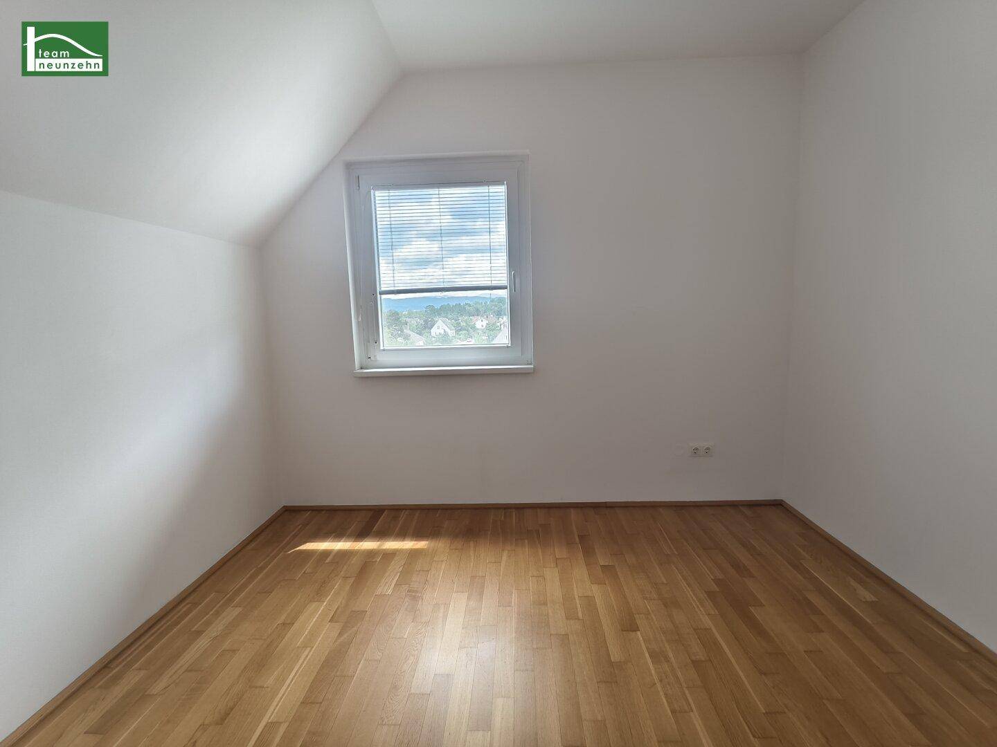 Gemütliches Zimmer mit Holzboden, Dachschräge und Fenster mit Ausblick.