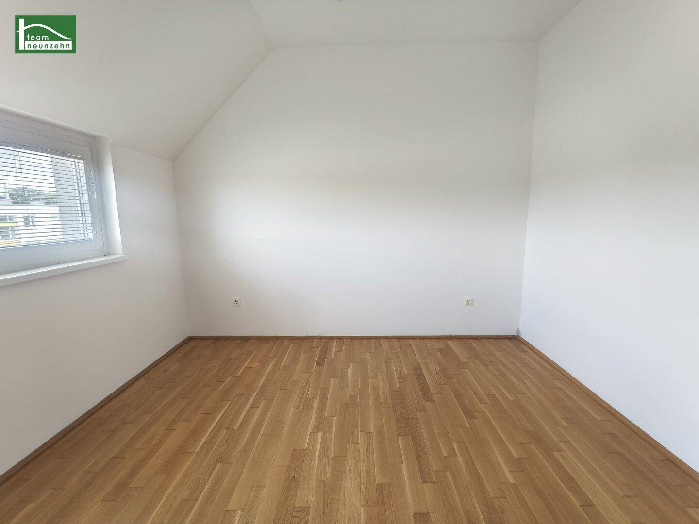 Ruhiges Zimmer mit Holzboden, weiß gestrichenen Wänden und Dachschräge.
