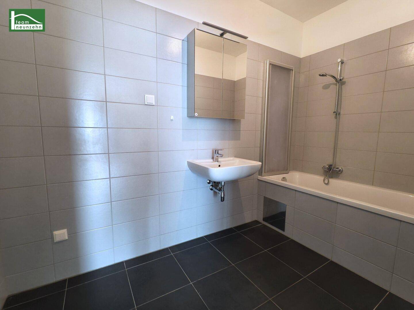 Modernes Badezimmer mit grauen Fliesen, Badewanne und Waschbecken mit Spiegelschrank.