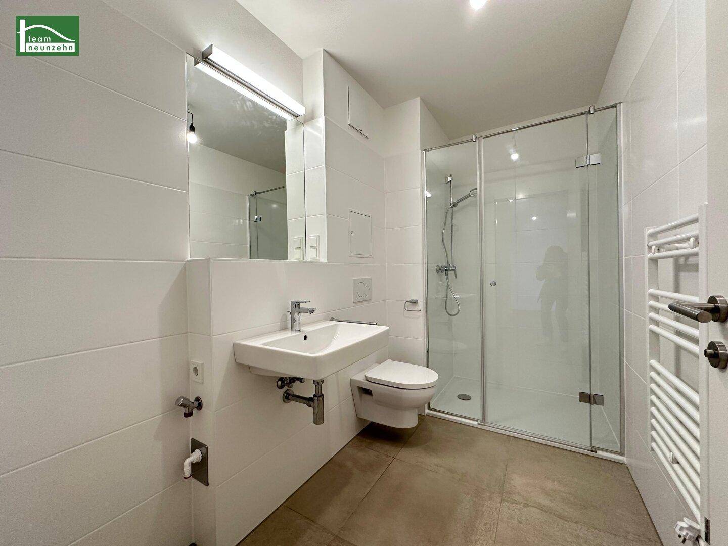 Modernes Badezimmer mit weißen Fliesen, Waschbecken, Toilette und begehbarer Dusche.