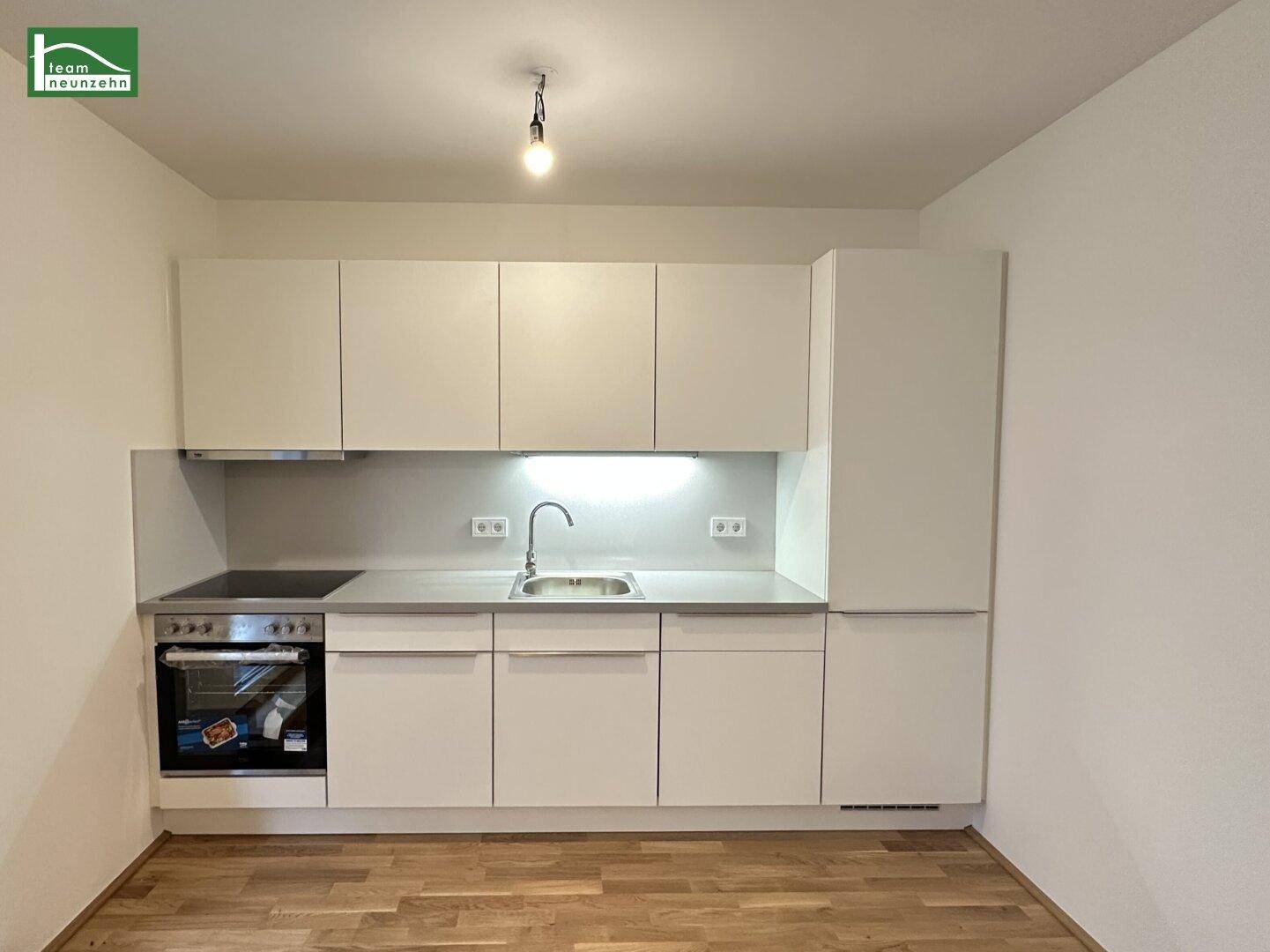 Moderne, kompakte Einbauküche mit weißen Schränken, Herd und Spüle.