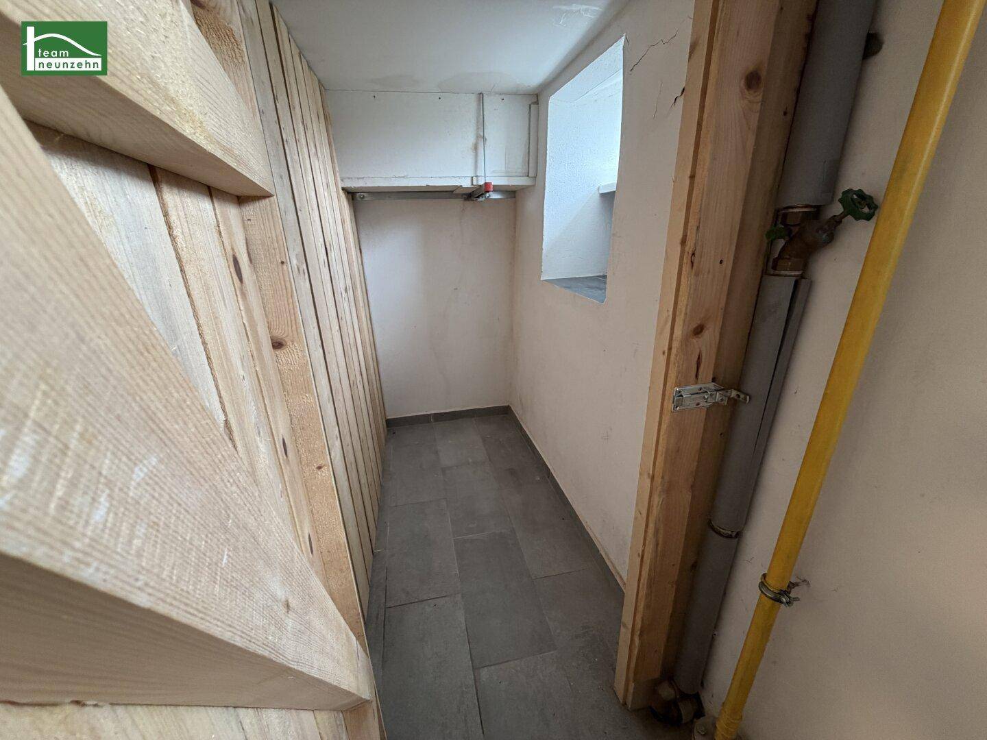 Unfertiger Kellerraum mit Holzverkleidung, Fliesenboden und sichtbaren Rohren sowie einem kleinen Fenster.