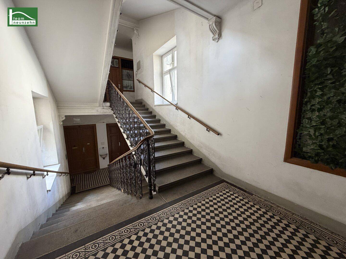 Historisches Treppenhaus mit schmiedeeisernem Geländer und gemusterten Fliesen im Eingangsbereich.