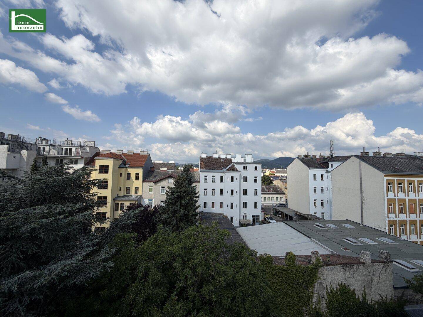 Panoramablick über die Dächer der Stadt mit grünen Bäumen und bewölktem Himmel.