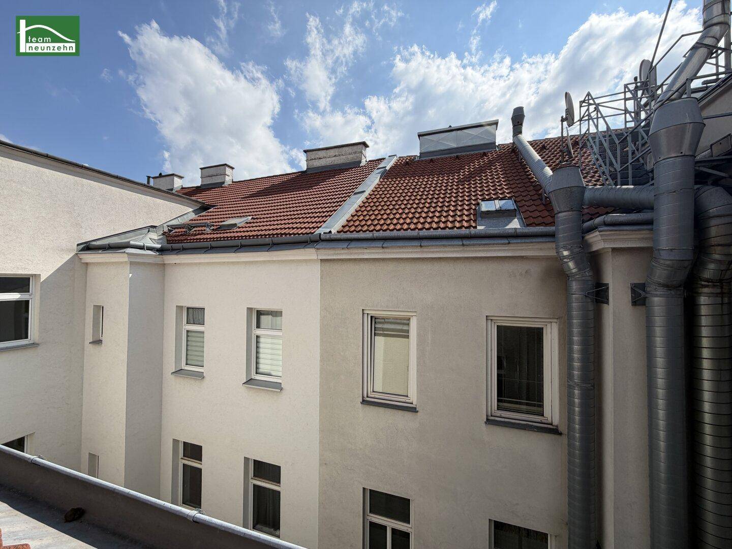 Rückansicht eines Gebäudes mit Ziegeldach und mehreren Fenstern, von einem Innenhof aus gesehen.