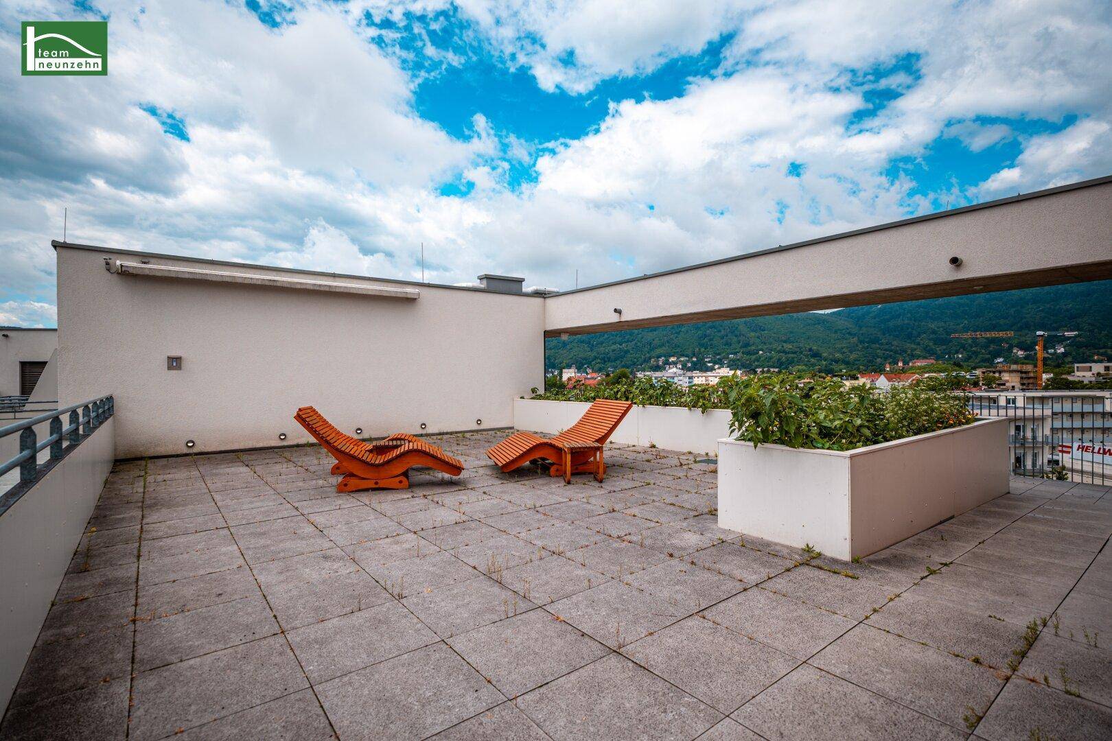 Weitläufige Dachterrasse mit Steinplatten und Holzliegen, ideal zum Entspannen unter freiem Himmel.