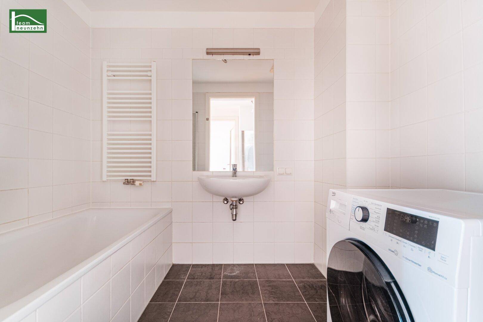 Funktionales Badezimmer mit Badewanne, Waschbecken, beheiztem Handtuchhalter und Waschmaschine.