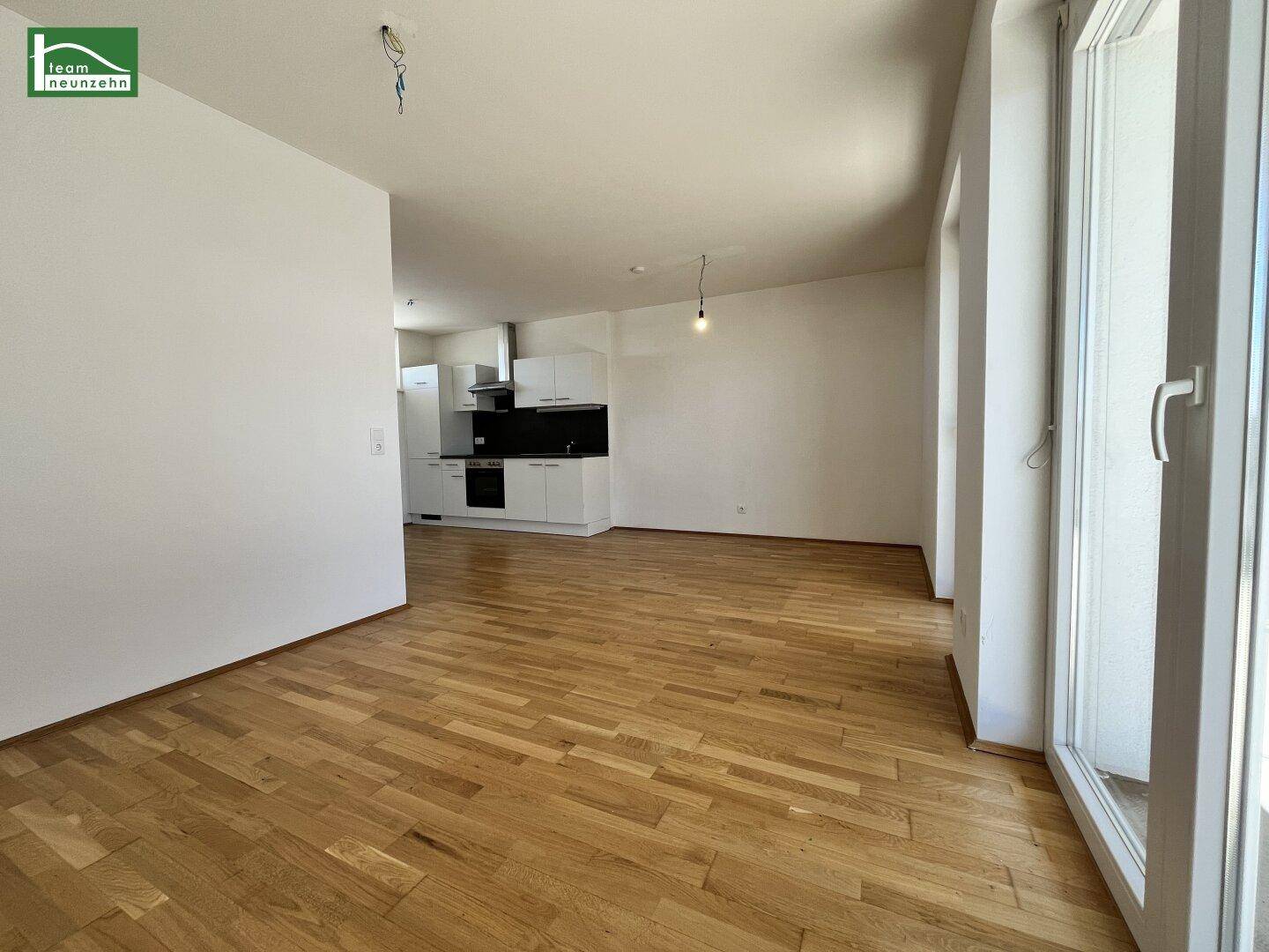 Offener Wohnbereich mit Parkettboden und Blick auf die vorbereitete Küchenzeile.