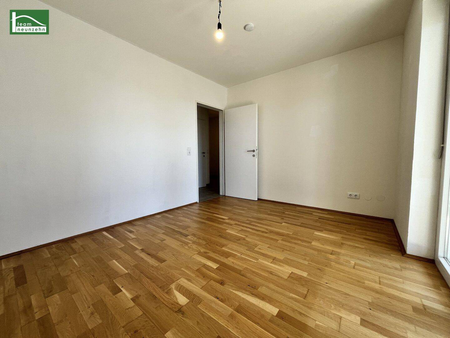 Geräumiges, leeres Zimmer mit Parkettboden und viel Tageslicht, ideal als Schlafzimmer.