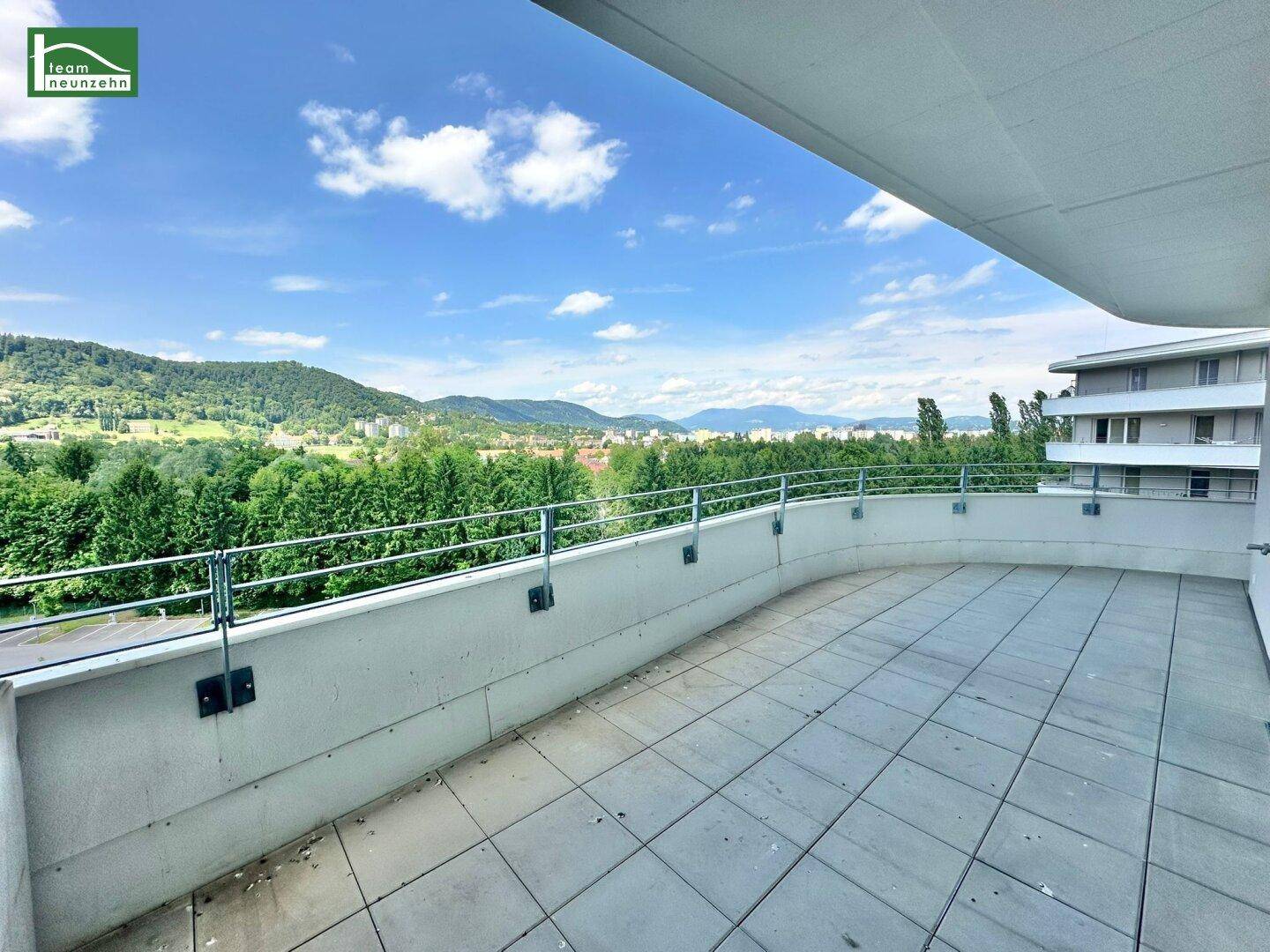 Großer, geschwungener Balkon mit Fliesenboden und Panoramablick auf die grüne Landschaft.