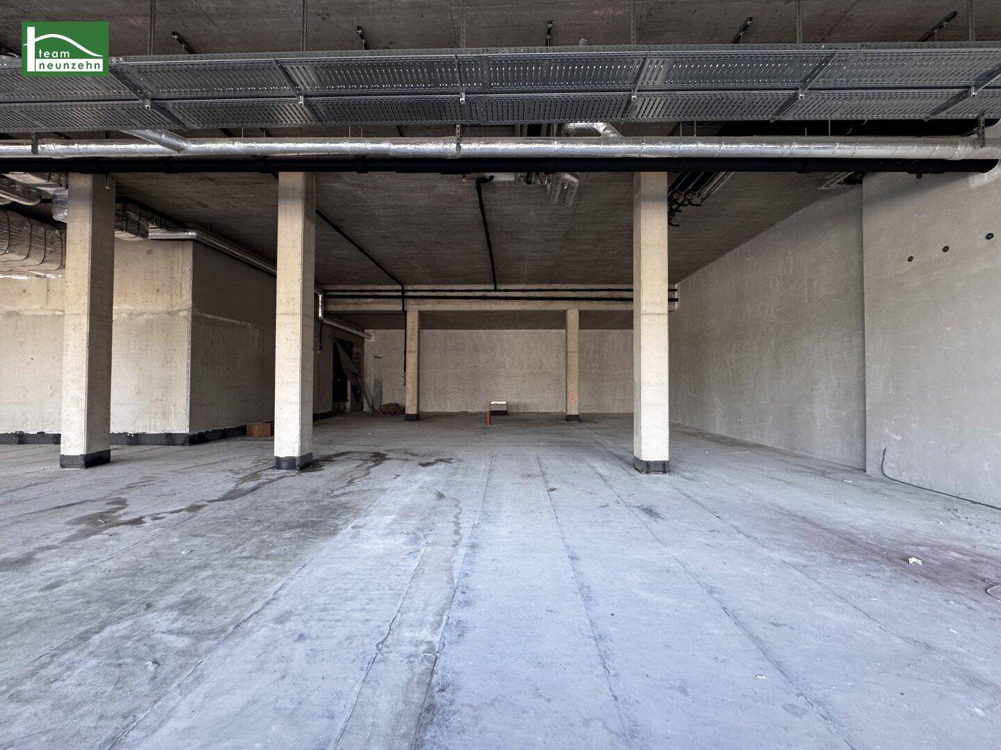 Großer, leerer Gewerberaum mit Betonboden, tragenden Säulen und sichtbaren Deckeninstallationen.