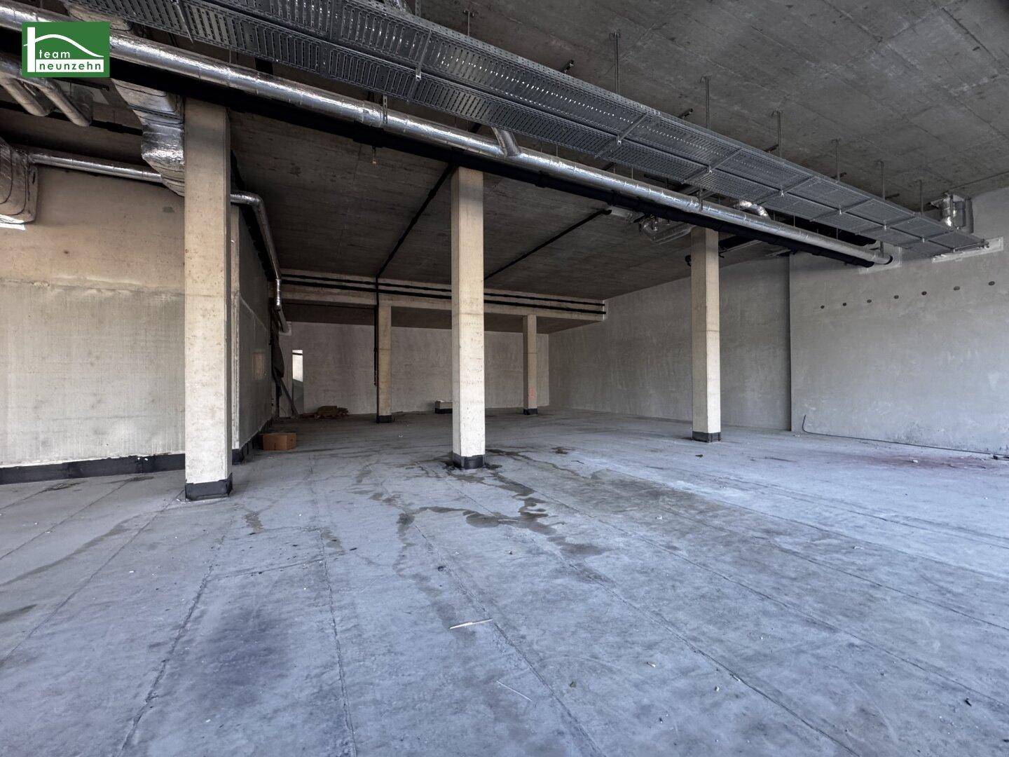 Leerer Gewerberaum mit Betonboden, Säulen und sichtbaren Lüftungsrohren an der Decke, bereit für den Ausbau.