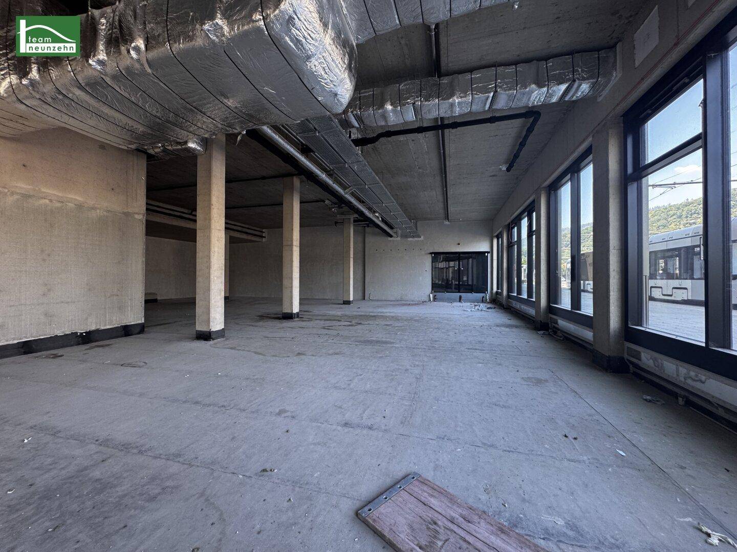 Großer, leerer Gewerberaum mit Betonboden, hohen Decken und großen Fenstern zur Straßenseite.