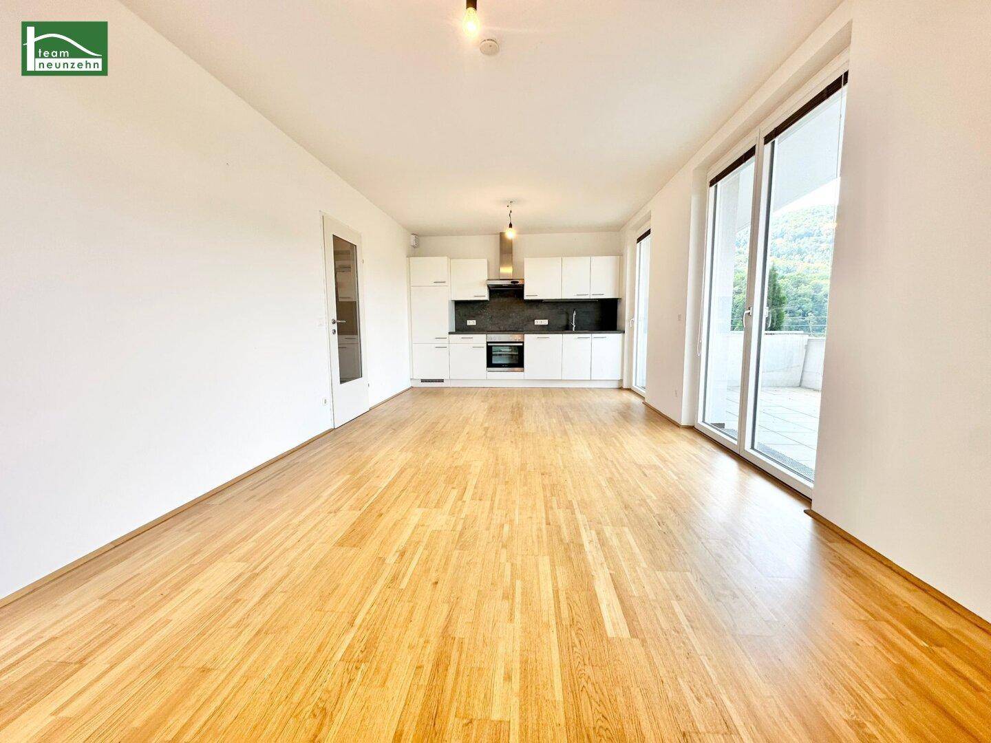 Geräumiger, leerer Wohn-Essbereich mit moderner Einbauküche und Zugang zur Terrasse.