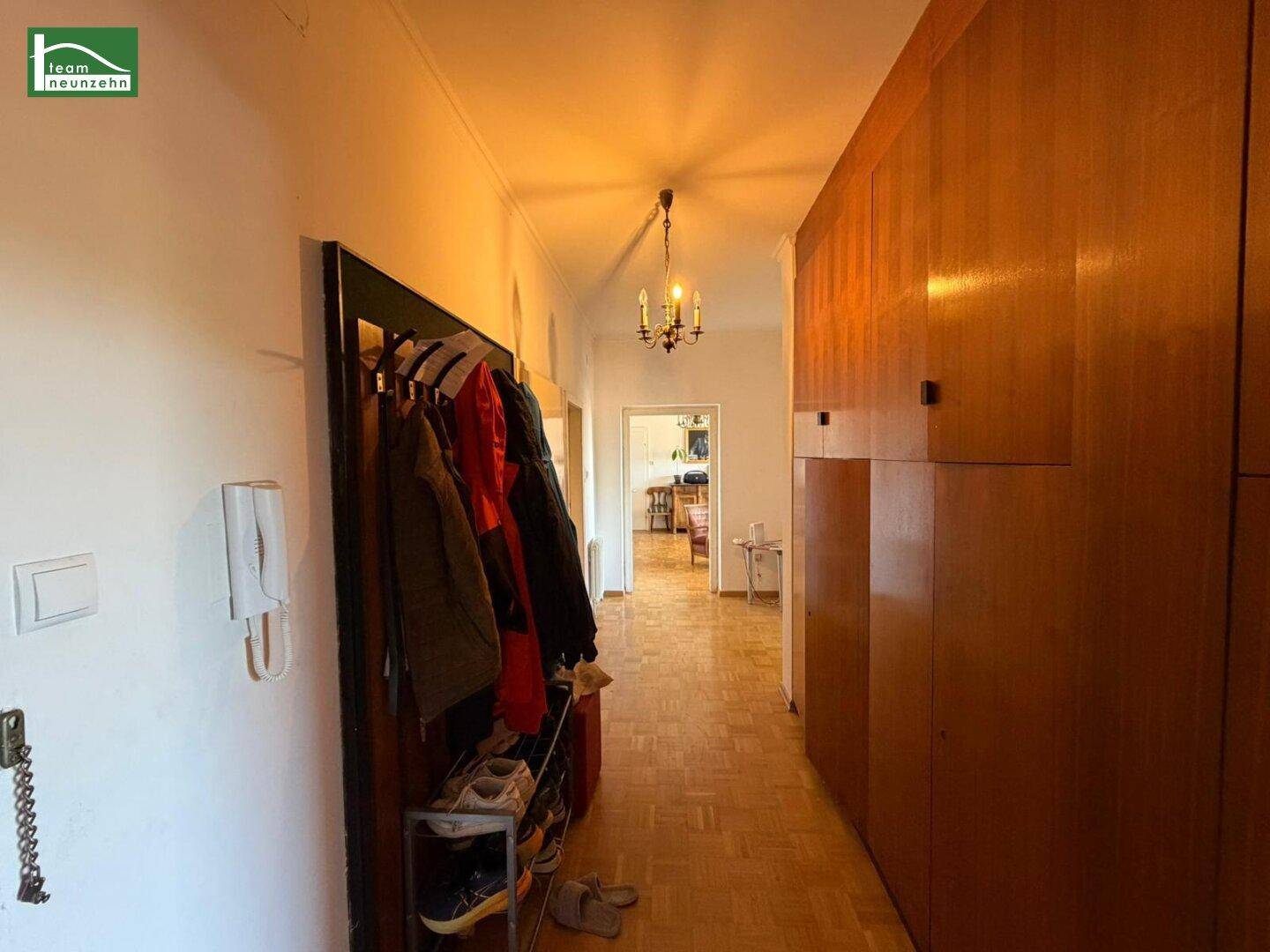 Langer Flur mit Holzvertäfelung, Parkettboden und Garderobe.
