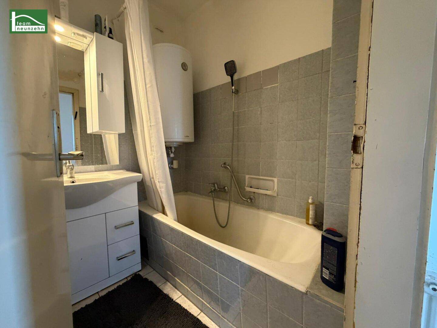 Badezimmer mit Badewanne, Waschbecken und hellgrauen Fliesen im 80er-Jahre-Stil.