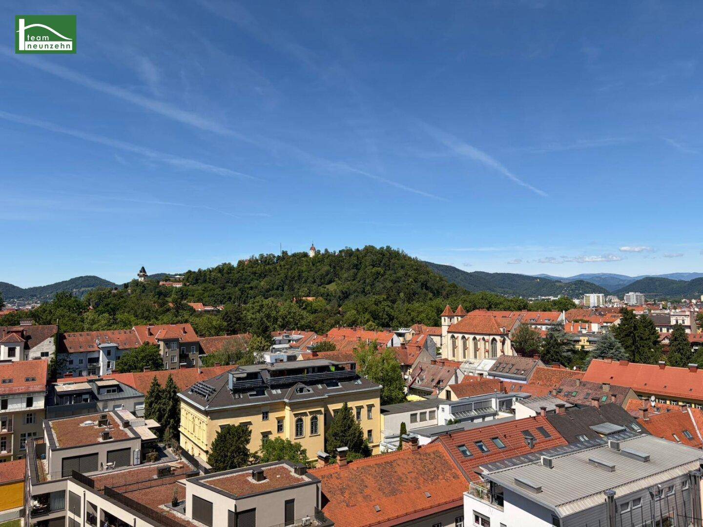 Panoramablick über die Stadt mit grünen Hügeln und historischen Gebäuden unter blauem Himmel.