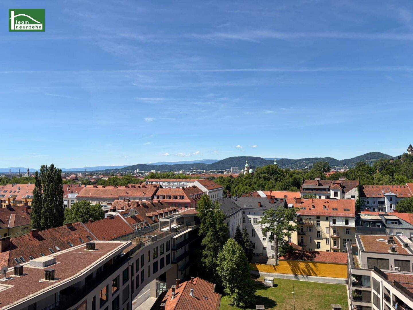 Weitläufiger Stadtblick mit vielen Dächern und bewaldeten Hügeln im Hintergrund.