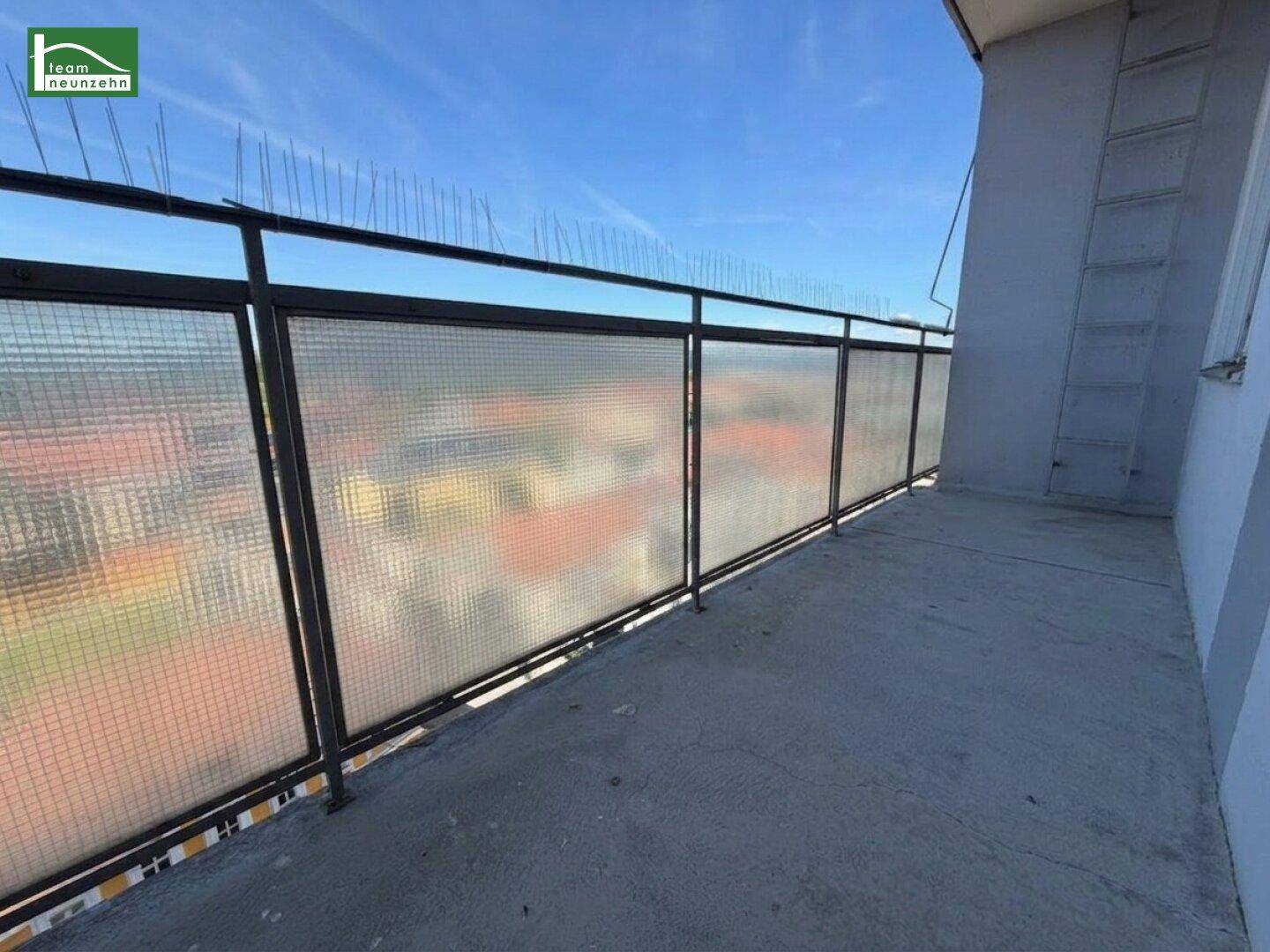 Balkon mit Gittergeländer und weitem Blick über die Stadt unter blauem Himmel.