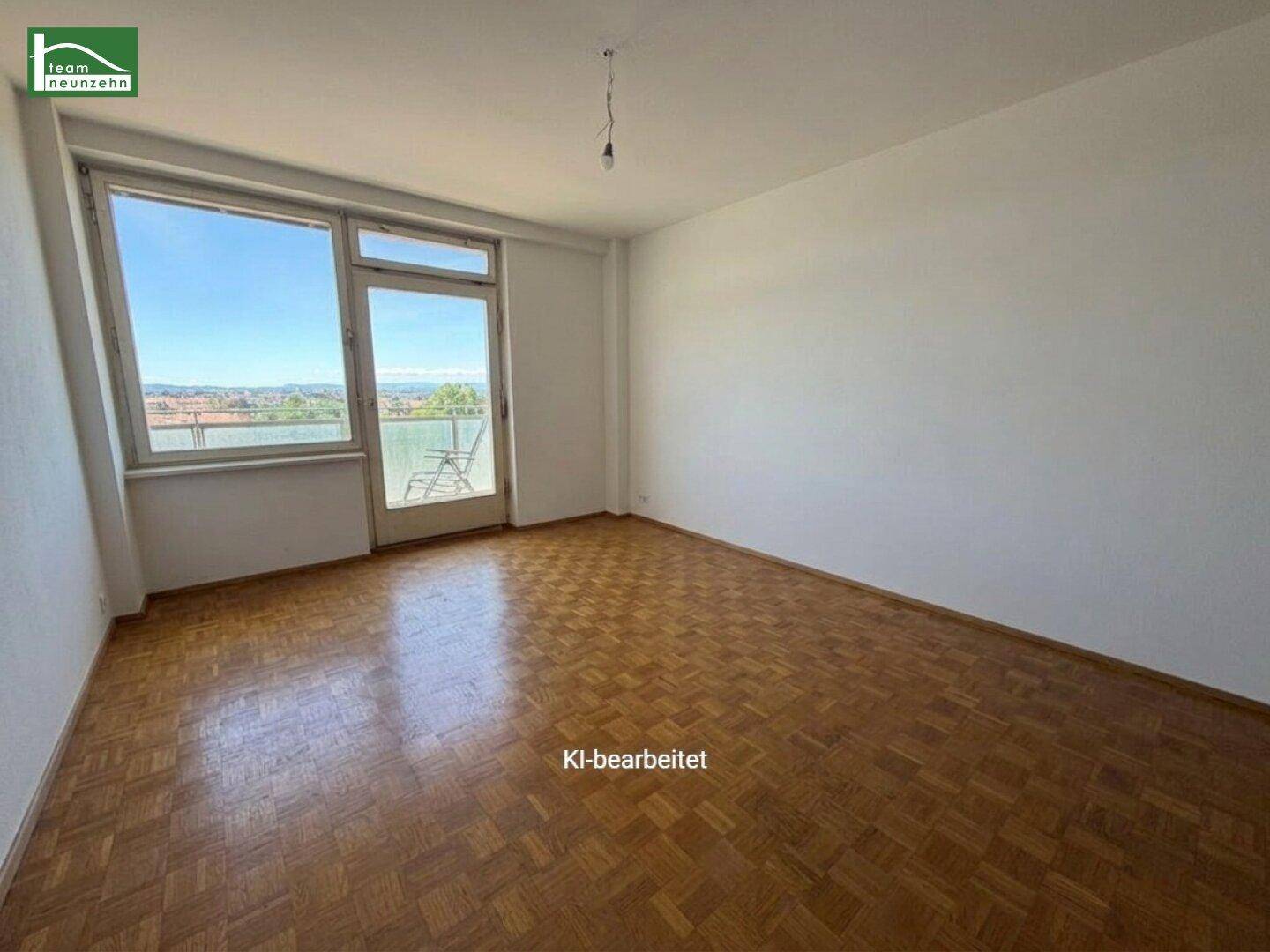 Leeres Zimmer mit Parkettboden, großen Fenstern und Zugang zum Balkon.