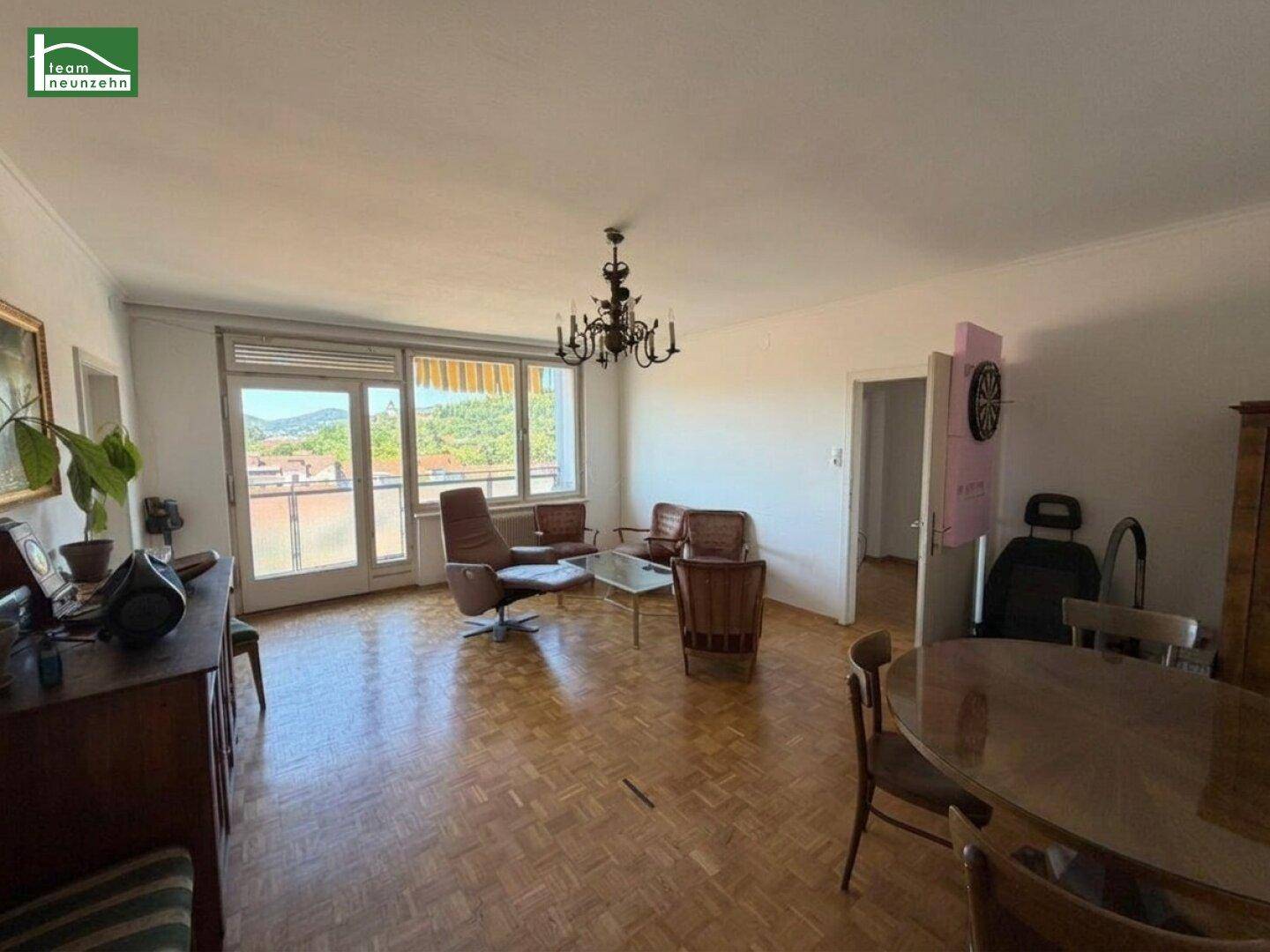 Heller Wohn-Essbereich mit Parkettboden, großem Fenster und Balkonzugang.