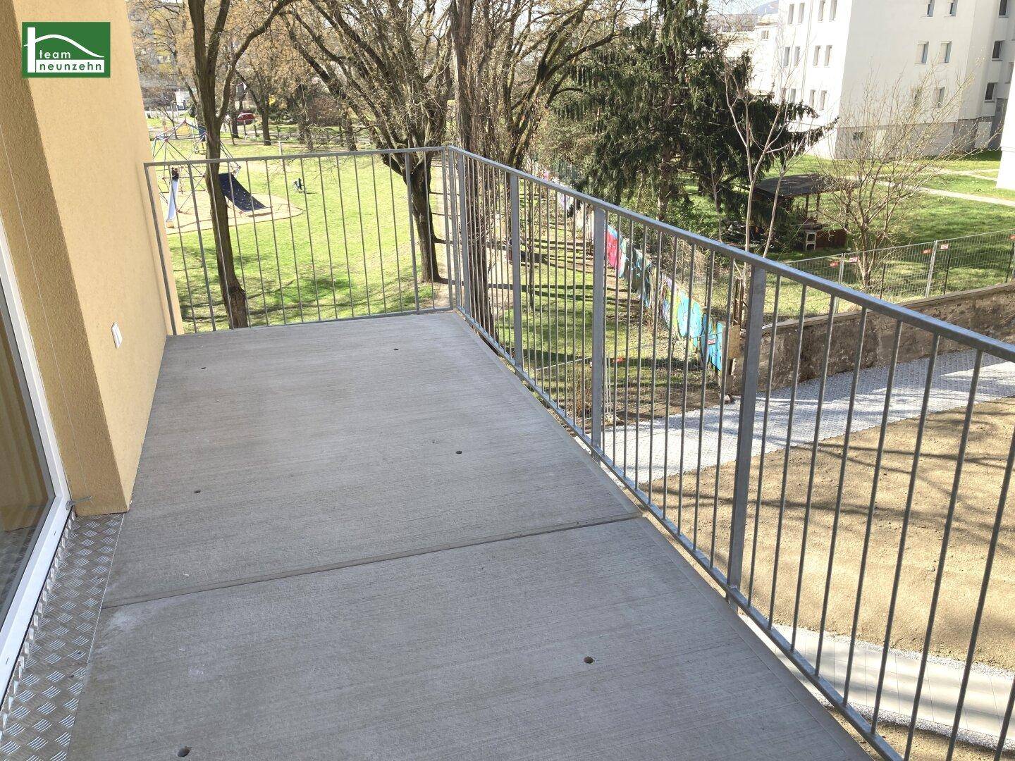 Geräumiger Balkon mit Metallgeländer und Blick auf eine Grünfläche mit Spielplatz.