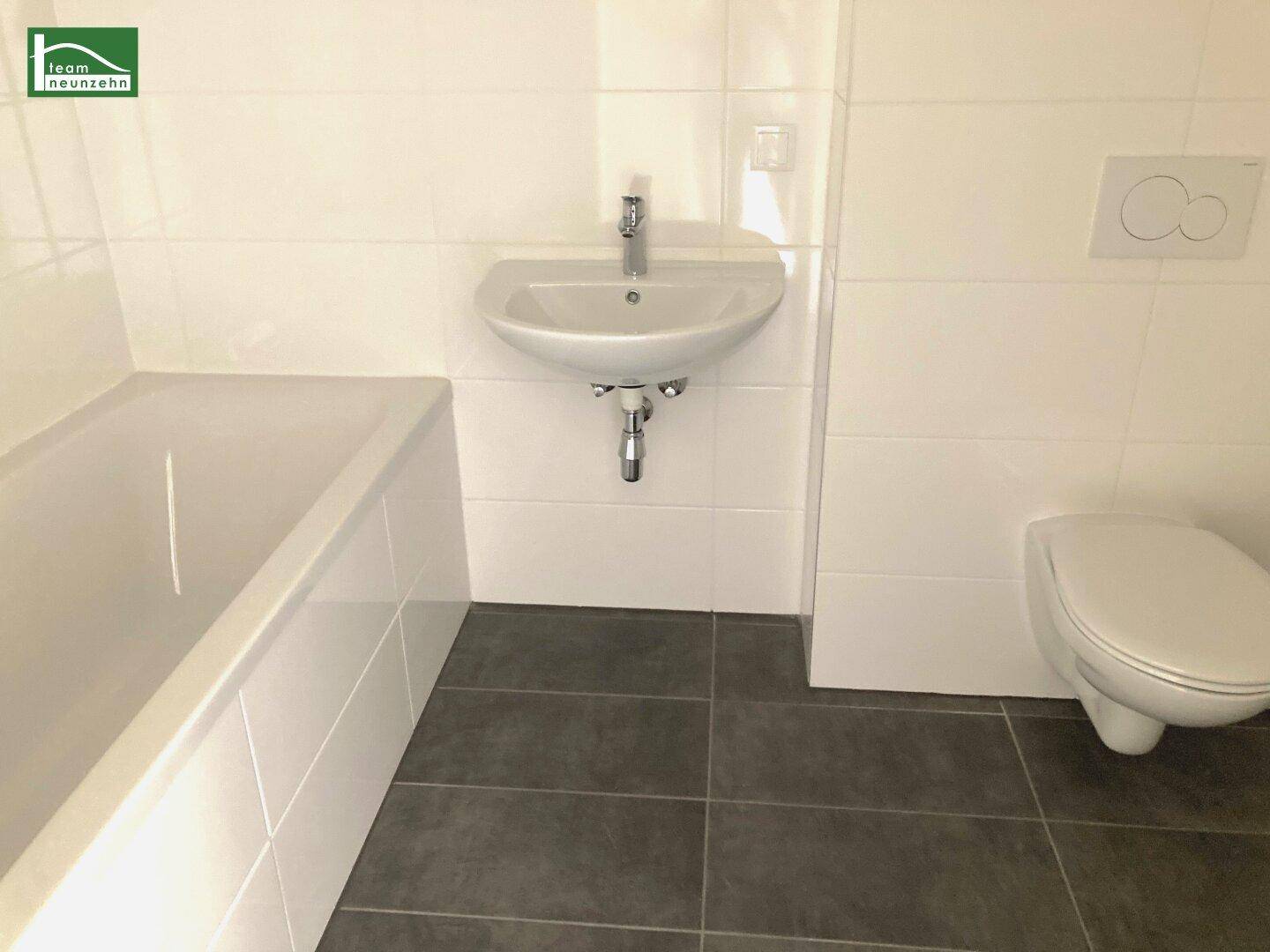 Modernes Badezimmer mit Badewanne, Waschbecken und Wand-WC, gefliest in Weiß und Grau.