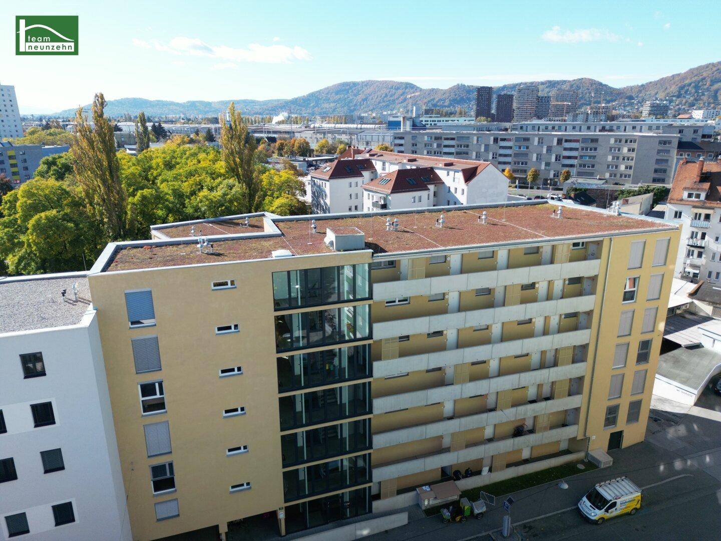 Luftaufnahme der Wohnanlage mit Flachdach und Blick auf die Stadt und Berge im Hintergrund.