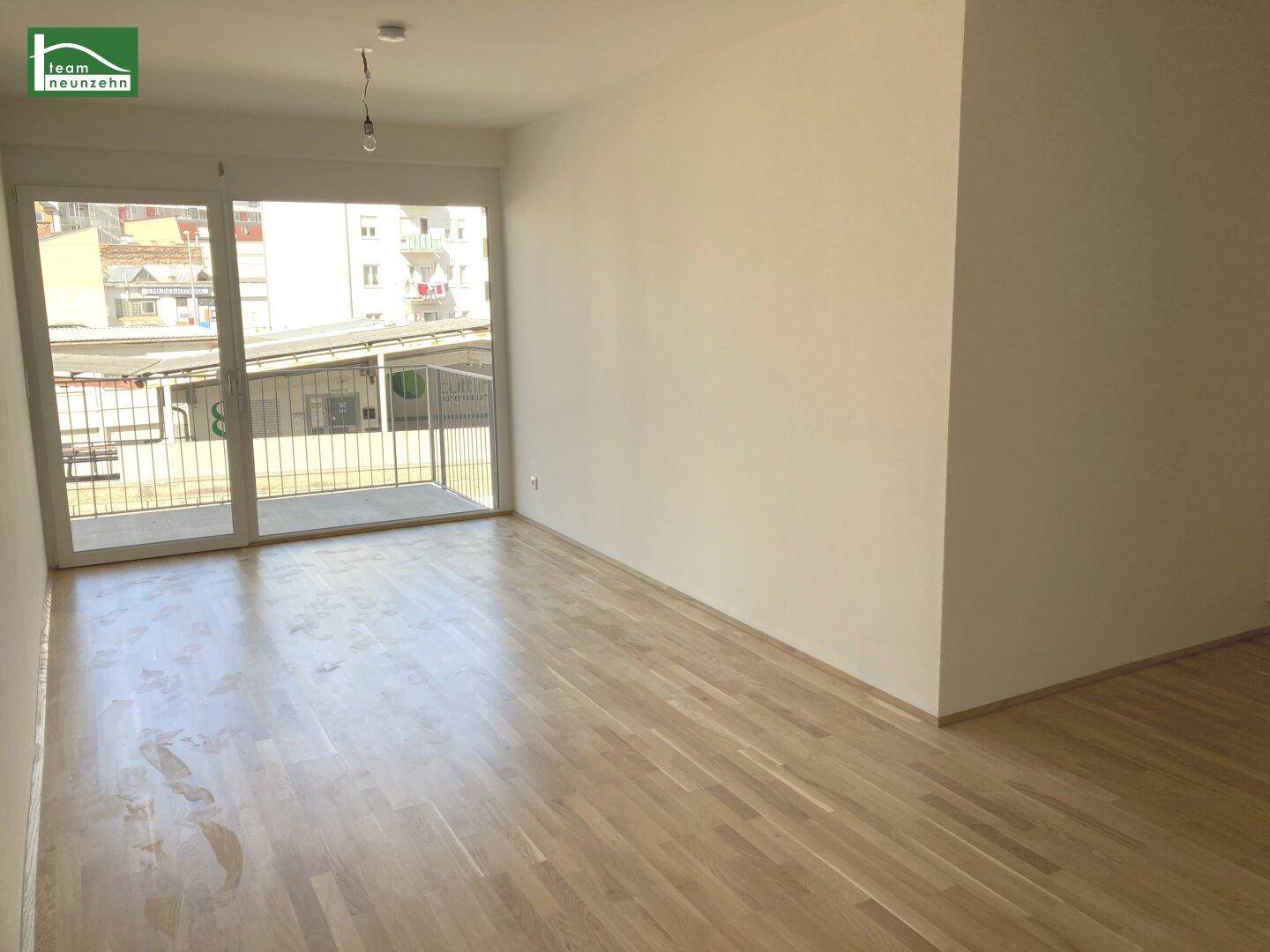 Geräumiges, leeres Wohnzimmer mit Parkettboden und großem Schiebefenster zum Balkon.