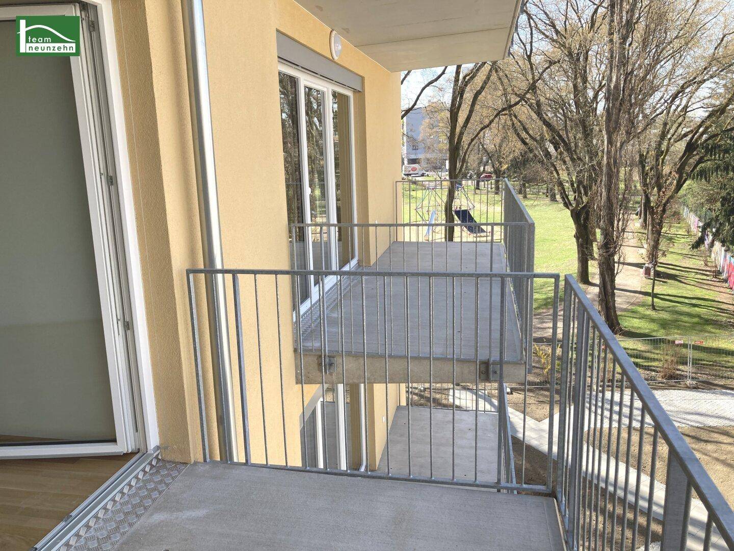 Kleiner Balkon mit Metallgeländer und Blick auf eine grüne Parkanlage mit Bäumen.