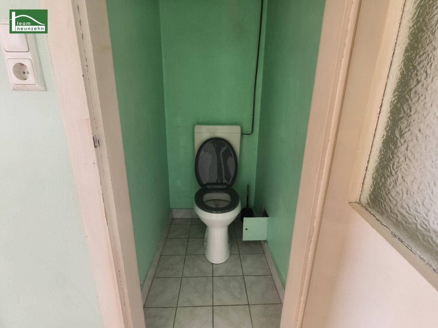 Separate Toilette mit grünen Wänden und Fliesenboden, einfach und funktional.