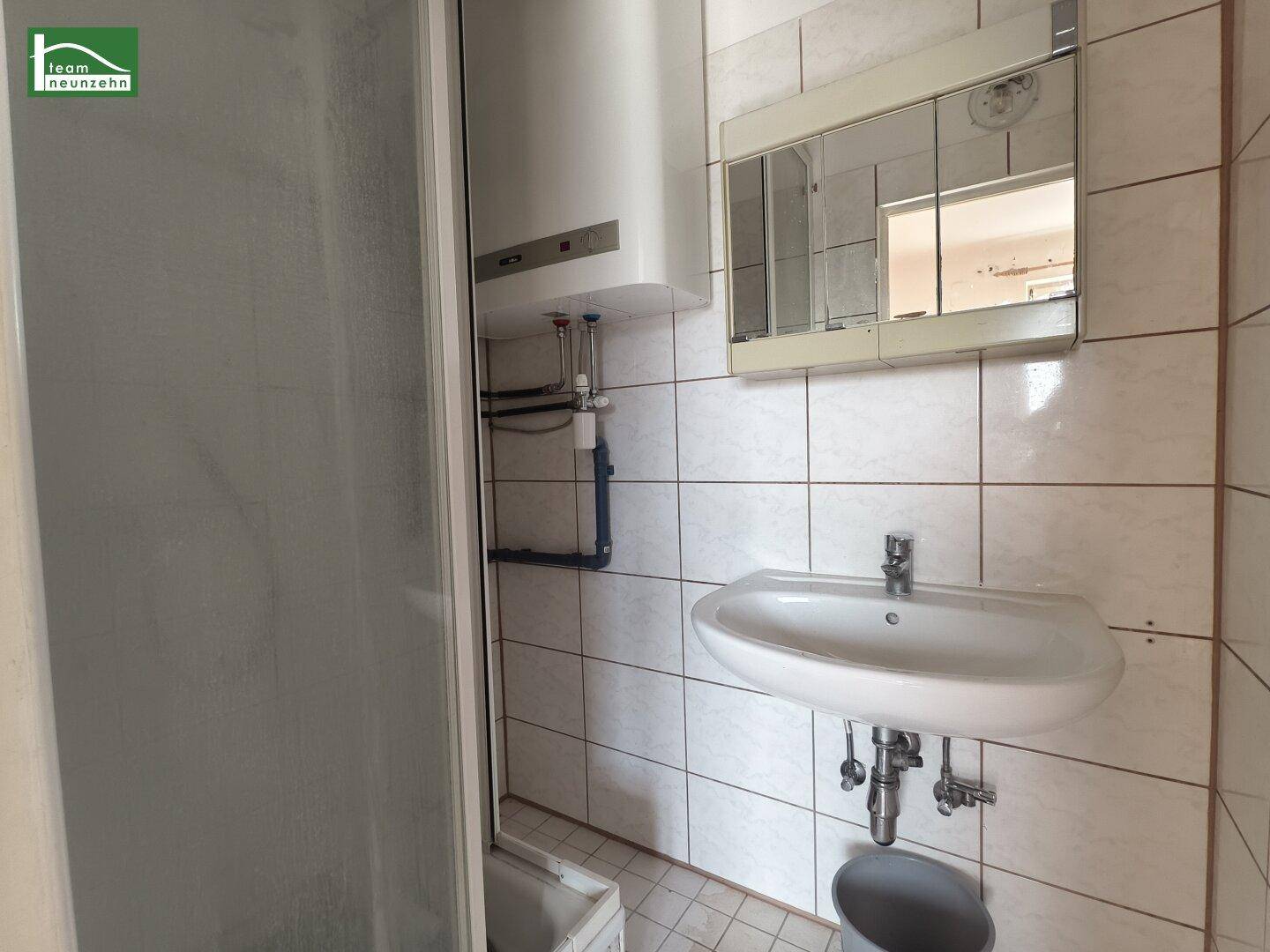 Badezimmer mit weißen Fliesen, Waschbecken, Spiegelschrank und Duschkabine.