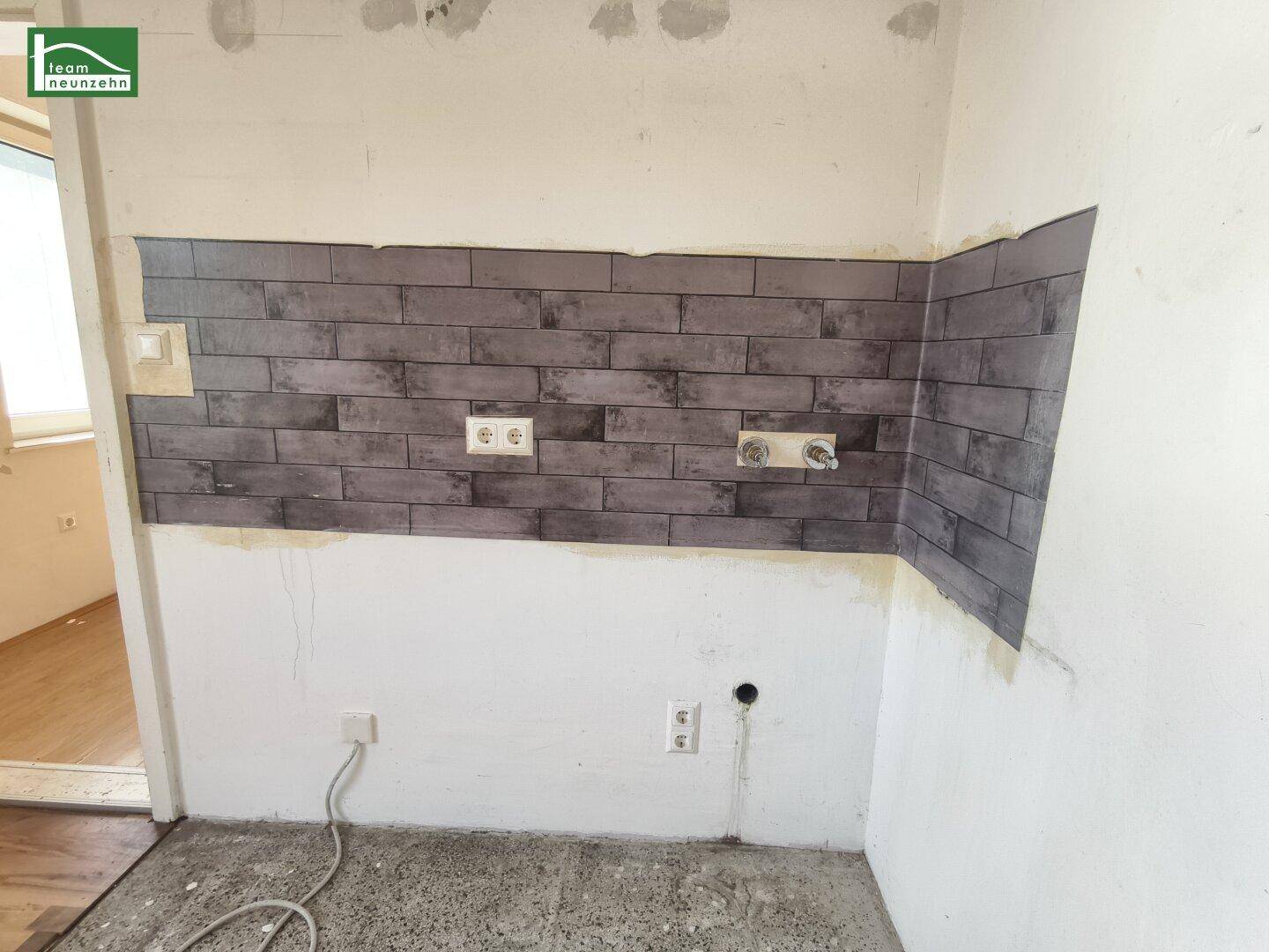 Detailansicht der Küchenwand mit Fliesenoptik, Steckdosen und Wasseranschlüssen für die Installation.