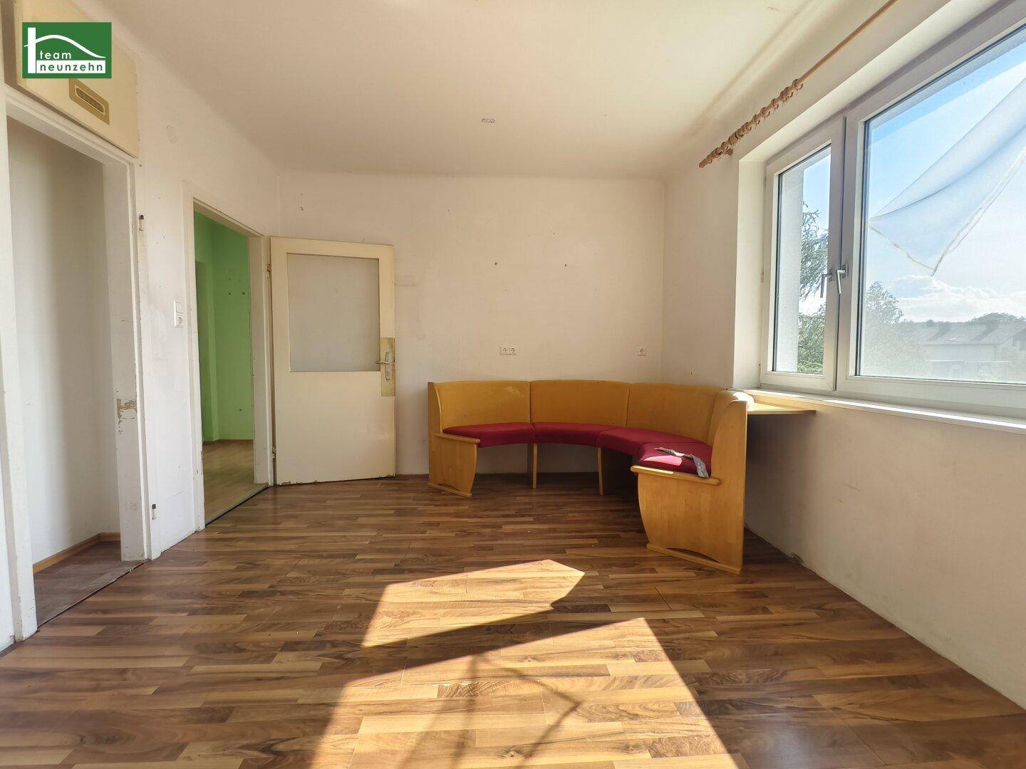Heller Wohnraum mit Laminatboden, großer Fensterfront und einer eingebauten Sitzbank.