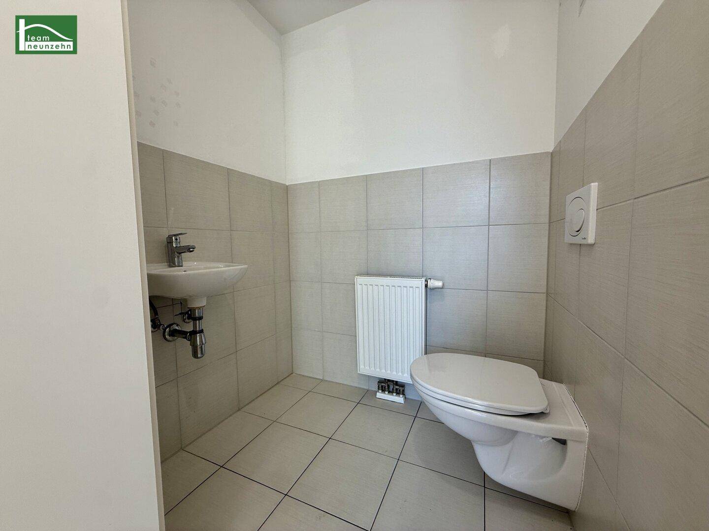 Separates Gäste-WC mit wandhängender Toilette, kleinem Waschbecken und Fliesen an den Wänden.