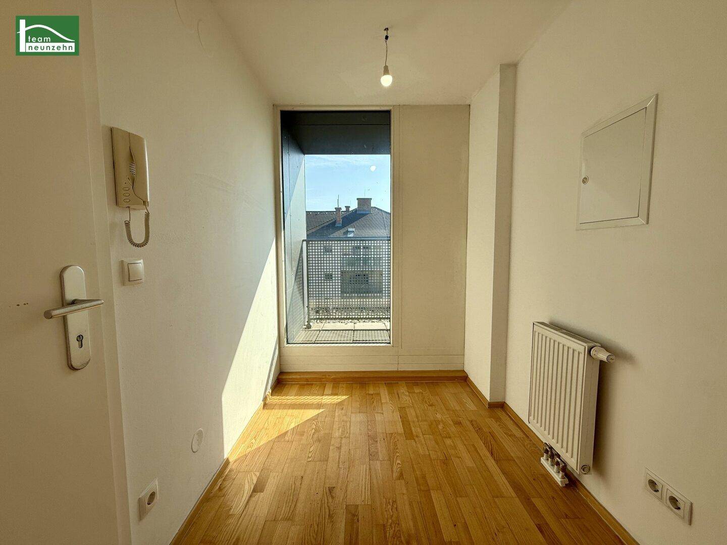 Kleiner Flur mit Parkettboden, Gegensprechanlage und einem französischen Balkon mit Blick nach draußen.