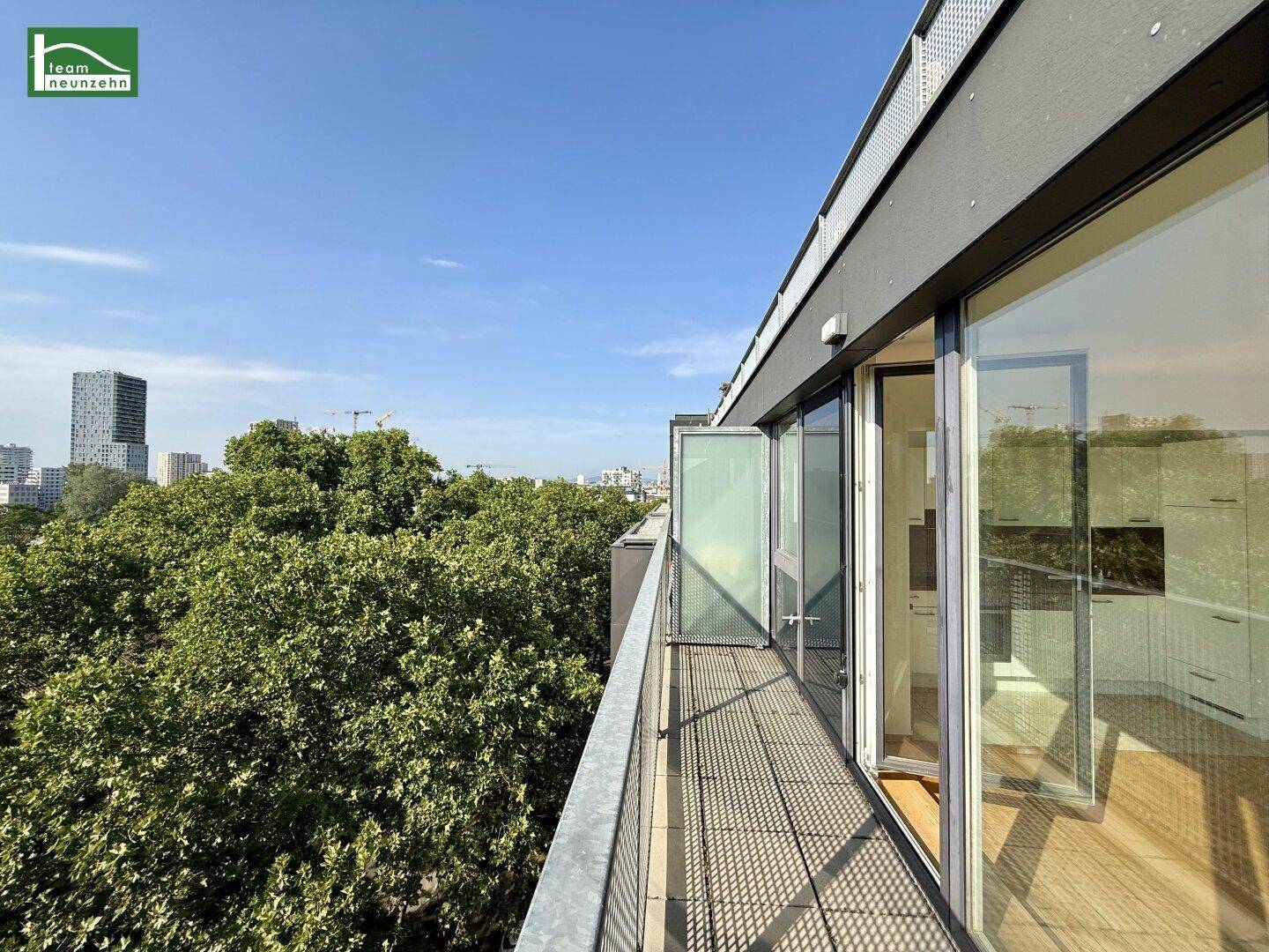 Geräumiger Balkon mit Metallboden, Blick auf grüne Bäume und die Stadtkulisse.