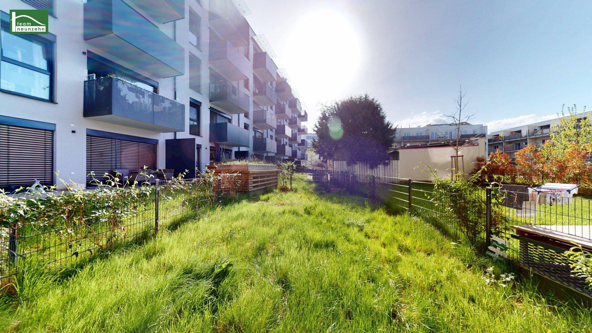 Grüne Gartenfläche vor einem modernen Wohngebäude mit Balkonen und Terrassen.
