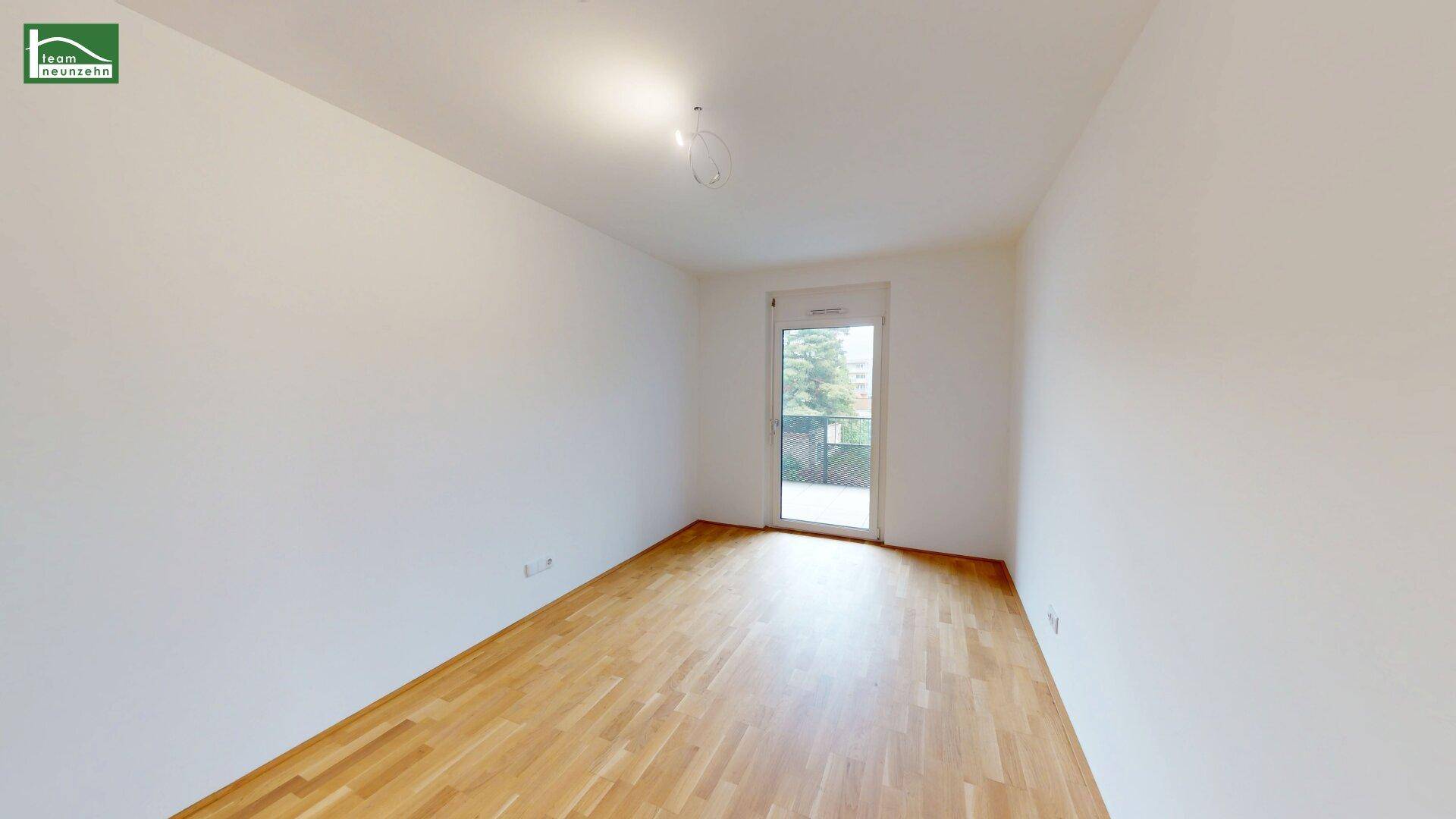Helles, leeres Schlafzimmer mit Holzboden und Zugang zu einem Balkon.